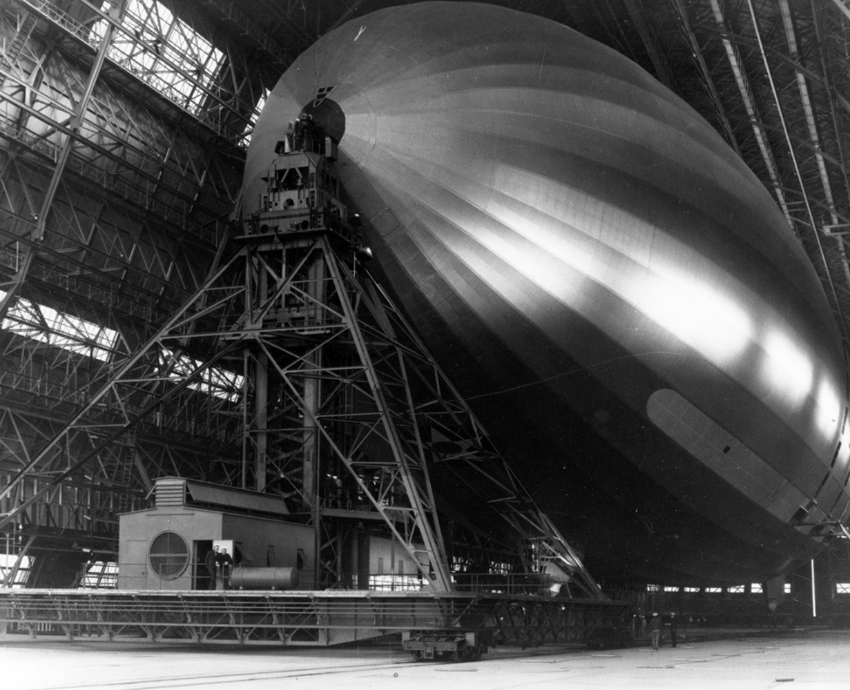 The USS Macon dirigible attached to a mooring mast inside Hangar 1. Light through the hangar windows reflects off of the silvery surface of the Macon.
