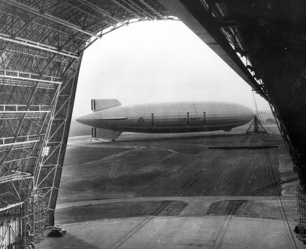 The USS Macon attached to its mooring mast. The full length view of the dirigible is taken from inside Hangar 1, through its huge open doors.
